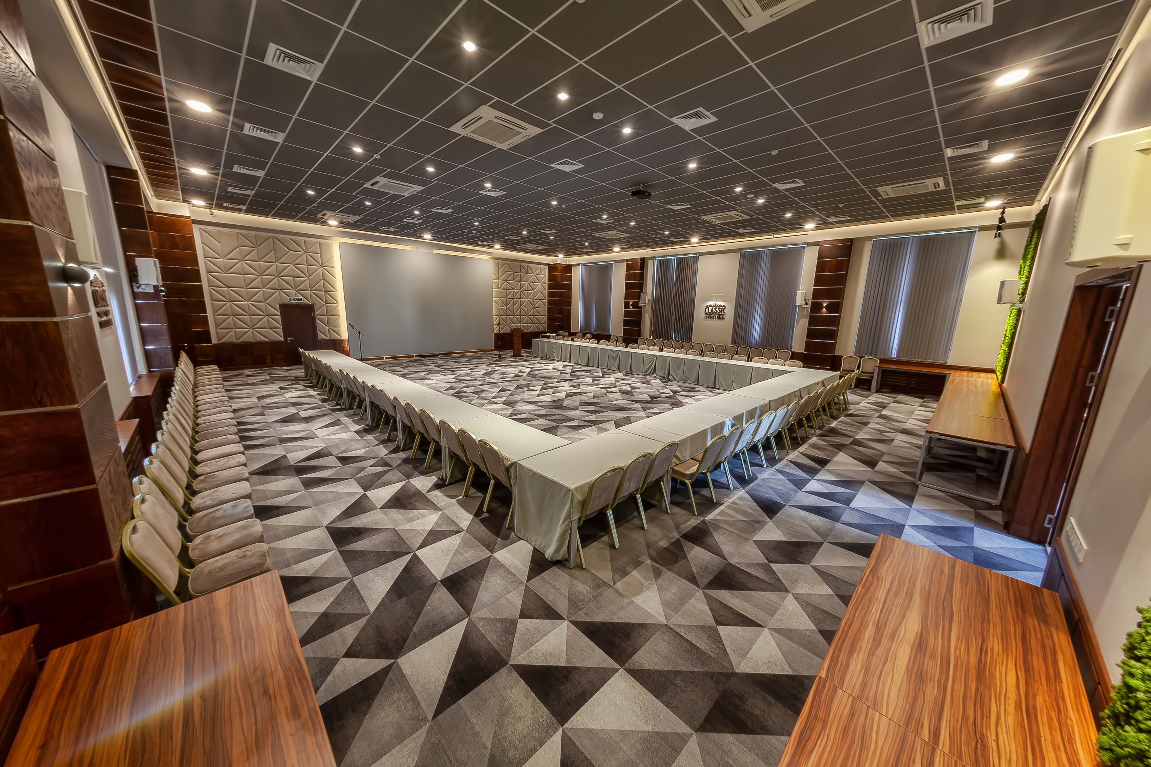 Un salón de conferencias con una larga mesa rodeada de sillas, una alfombra estampada y un diseño moderno de techo.