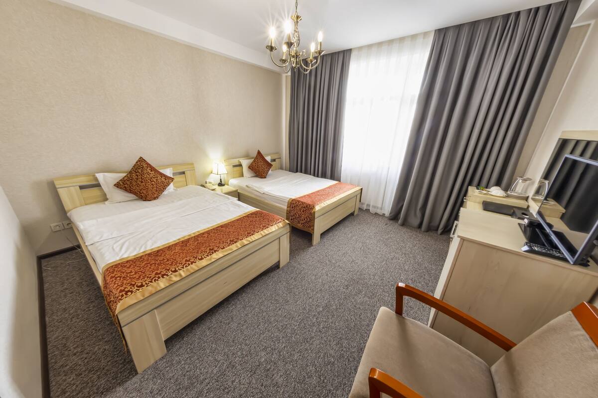 A hotel room with two beds, a desk, a chair, a TV, and a chandelier.