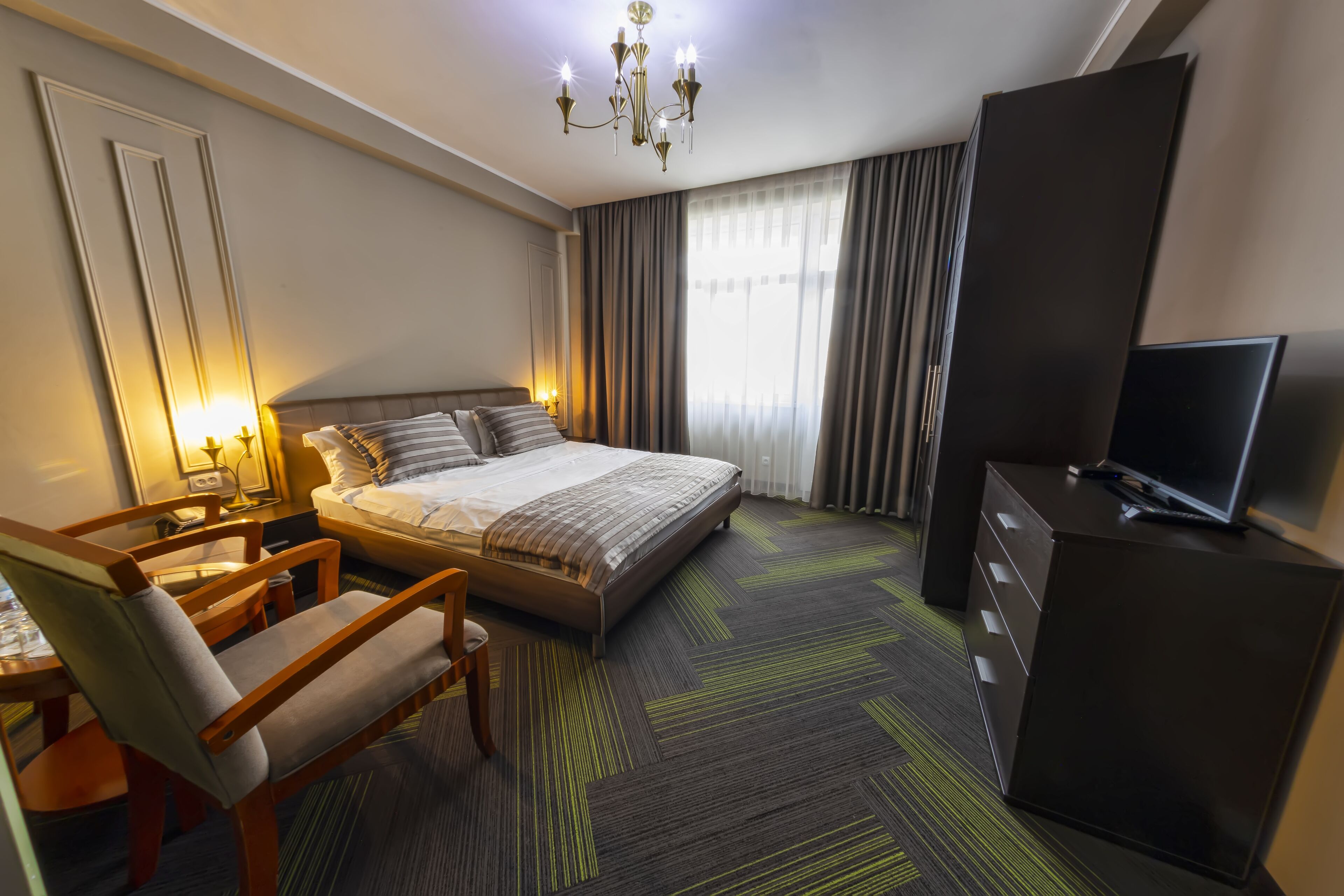 A hotel room with a bed, a desk, a chair, a television, and a wardrobe.