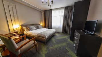 A hotel room with a bed, a desk, a chair, a television, and a wardrobe.
