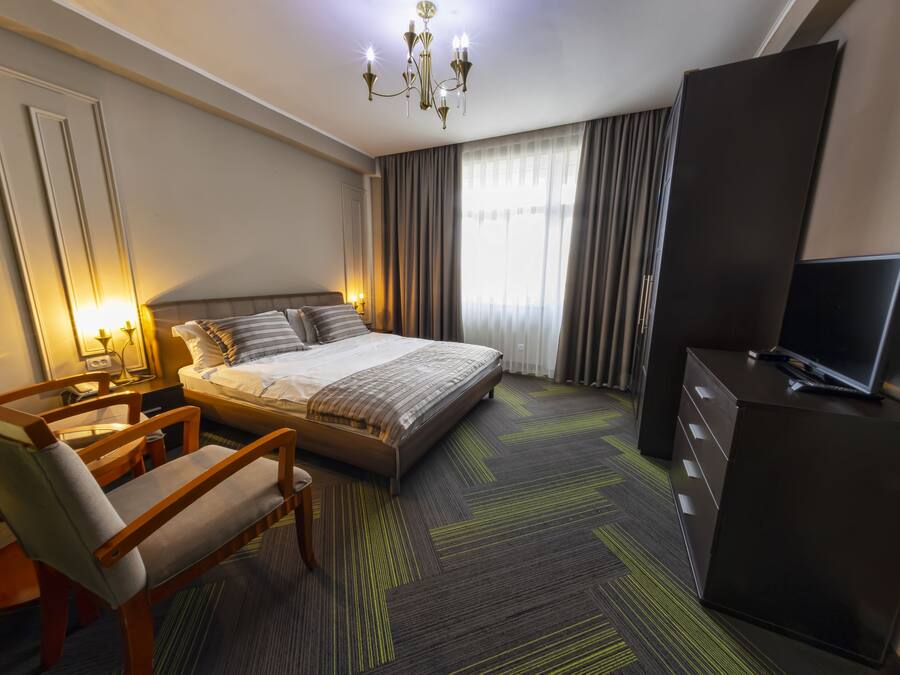 A hotel room with a bed, a desk, a chair, a television, and a wardrobe.