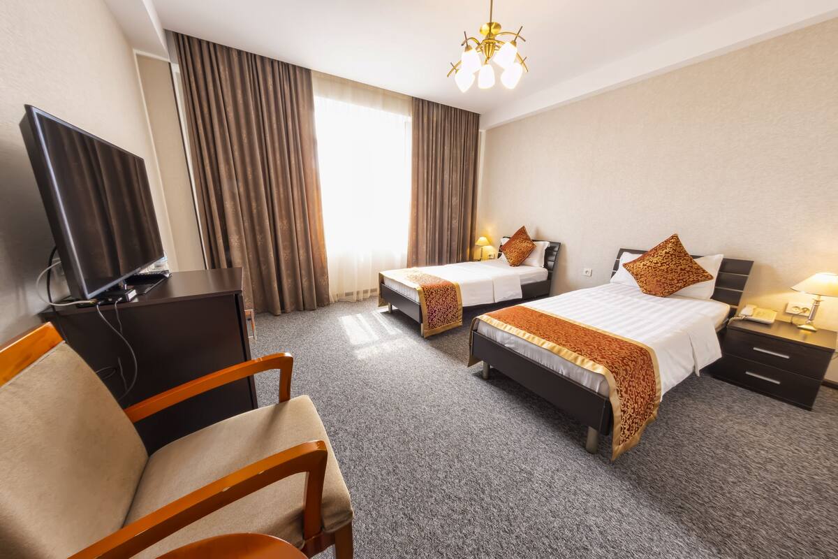 A hotel room with two beds, a desk, a television, and a chair.