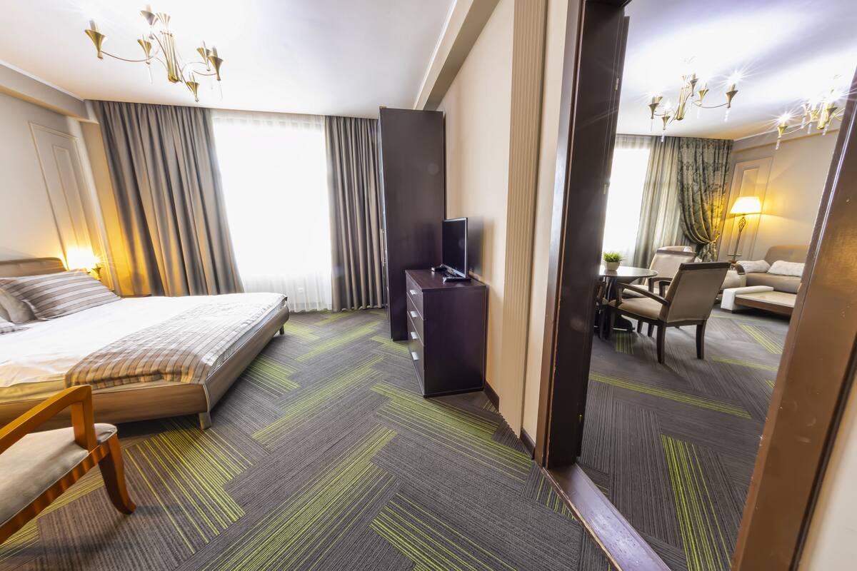A hotel room with a bed, a desk, a chair, a sofa, and a lamp.