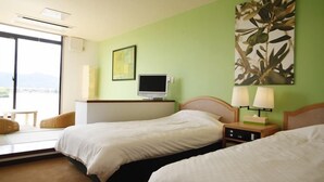 Quarto de hotel com duas camas, televisão, escrivaninha, cadeira e vista para o exterior.