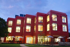 Een modern rood gebouw met veel ramen en buitenzitplaatsen.