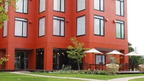 A multi-story building with a red facade, a paved pathway, and outdoor seating area. - Lake Side Hotel & Restaurant Little White Flower (Kyotango)
