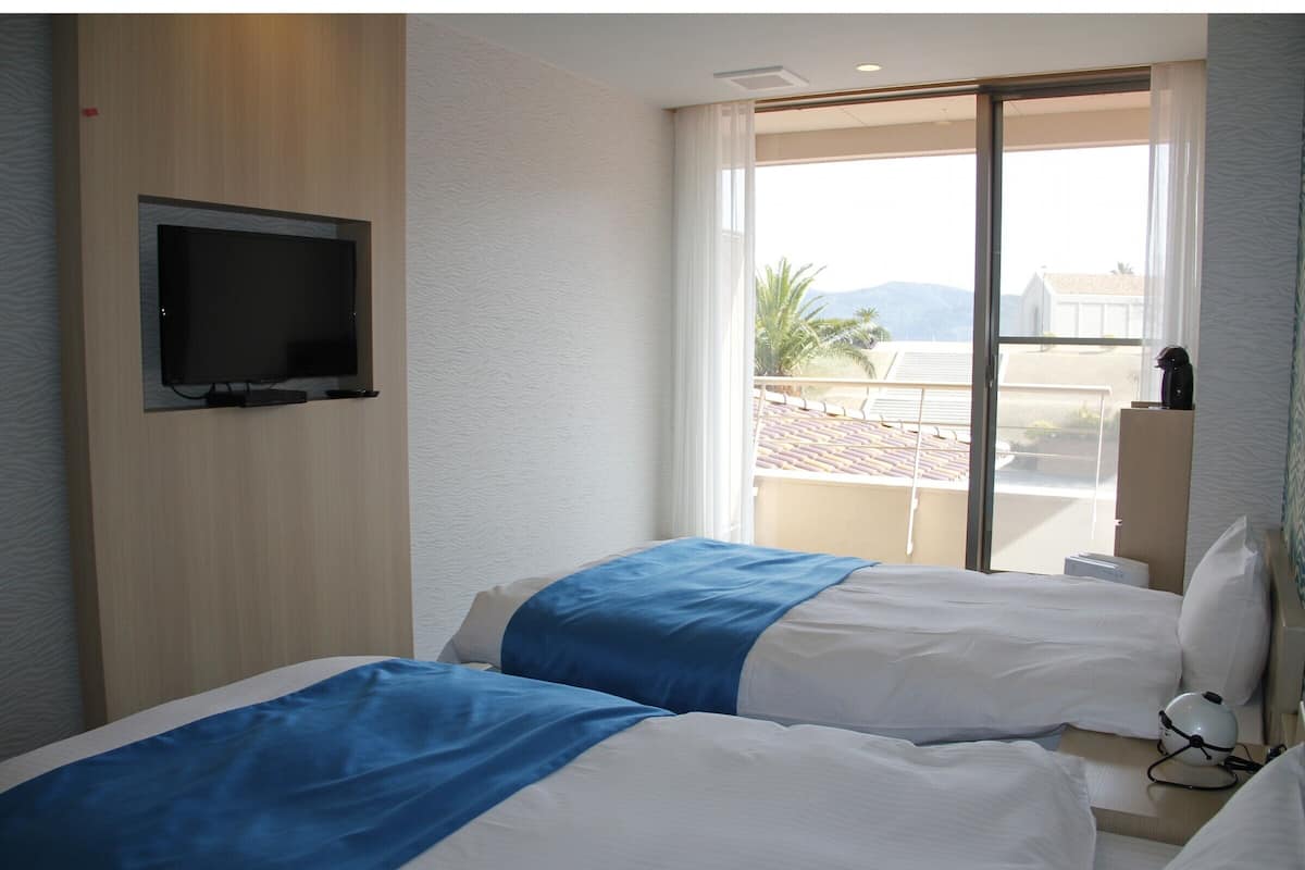 Une chambre d’hôtel avec deux lits, un téléviseur fixé au mur et une grande fenêtre donnant sur l’extérieur.