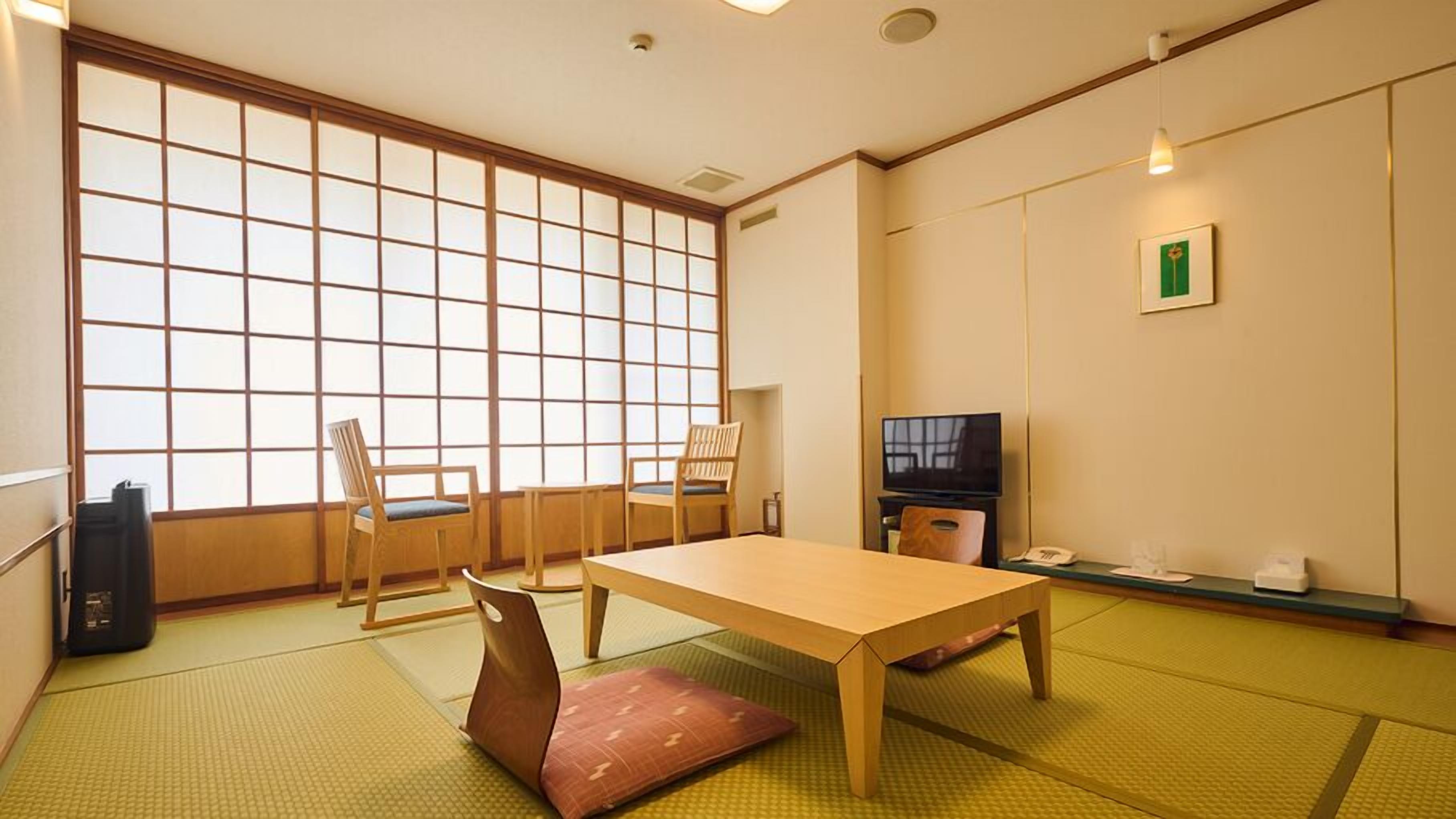 A traditional Japanese room with tatami flooring, a low table, wooden chairs, a television, and a sliding door.