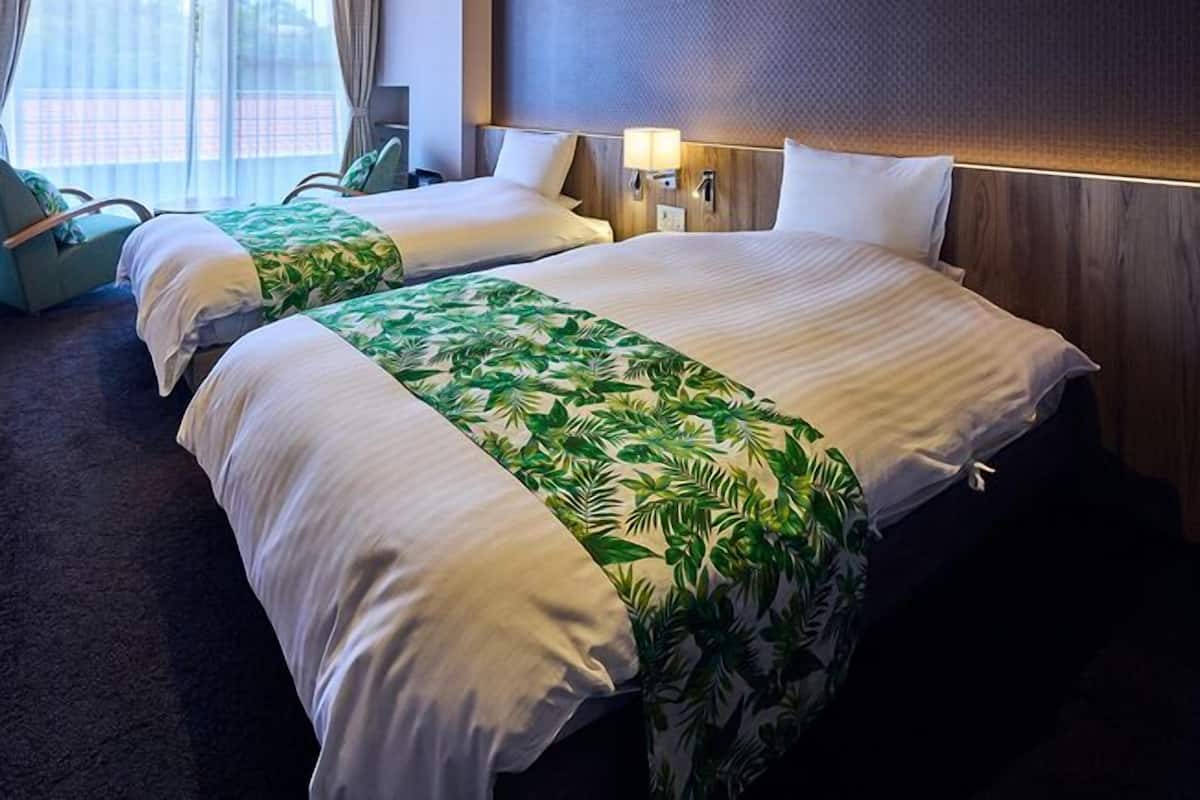 Une chambre d’hôtel avec deux lits, une fenêtre avec des rideaux, une chaise et une lampe fixée au mur.
