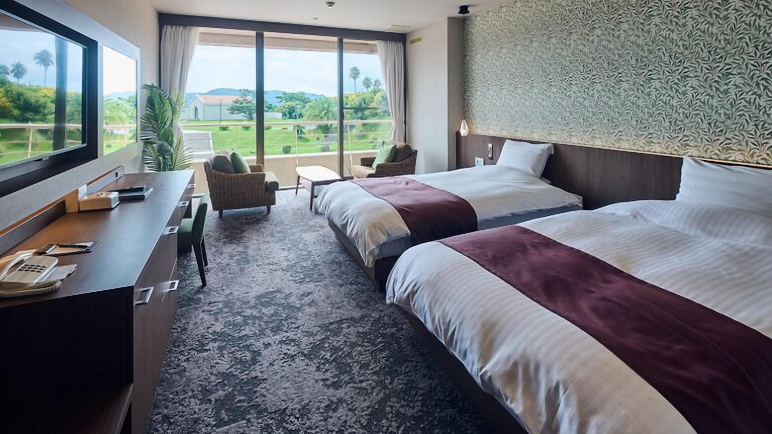 A hotel room with two beds, a desk with a phone, and a view of greenery outside.