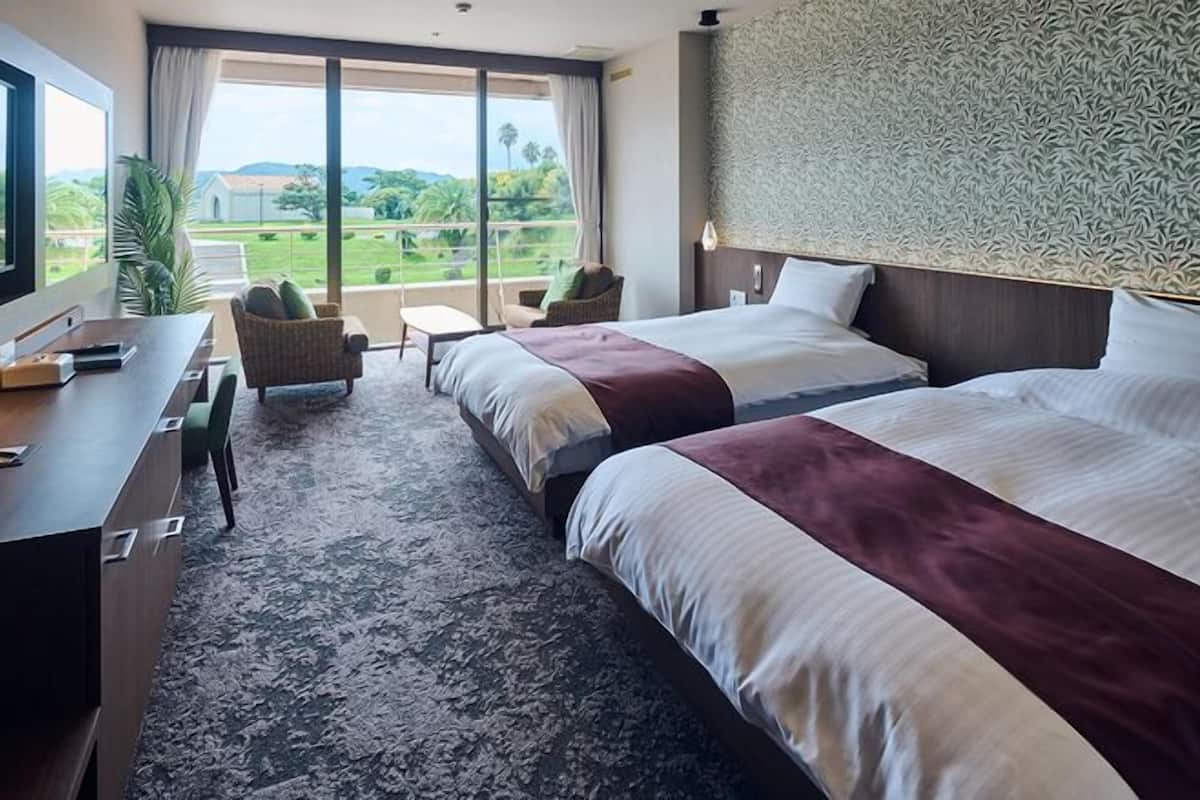 Une chambre d’hôtel avec deux lits, un bureau avec un téléphone et une vue sur la verdure environnante.