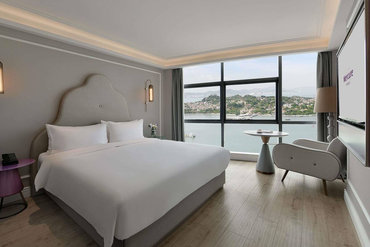 Une chambre d’hôtel avec un grand lit, une petite table, une chaise, une table de chevet et une vue sur une étendue d’eau.