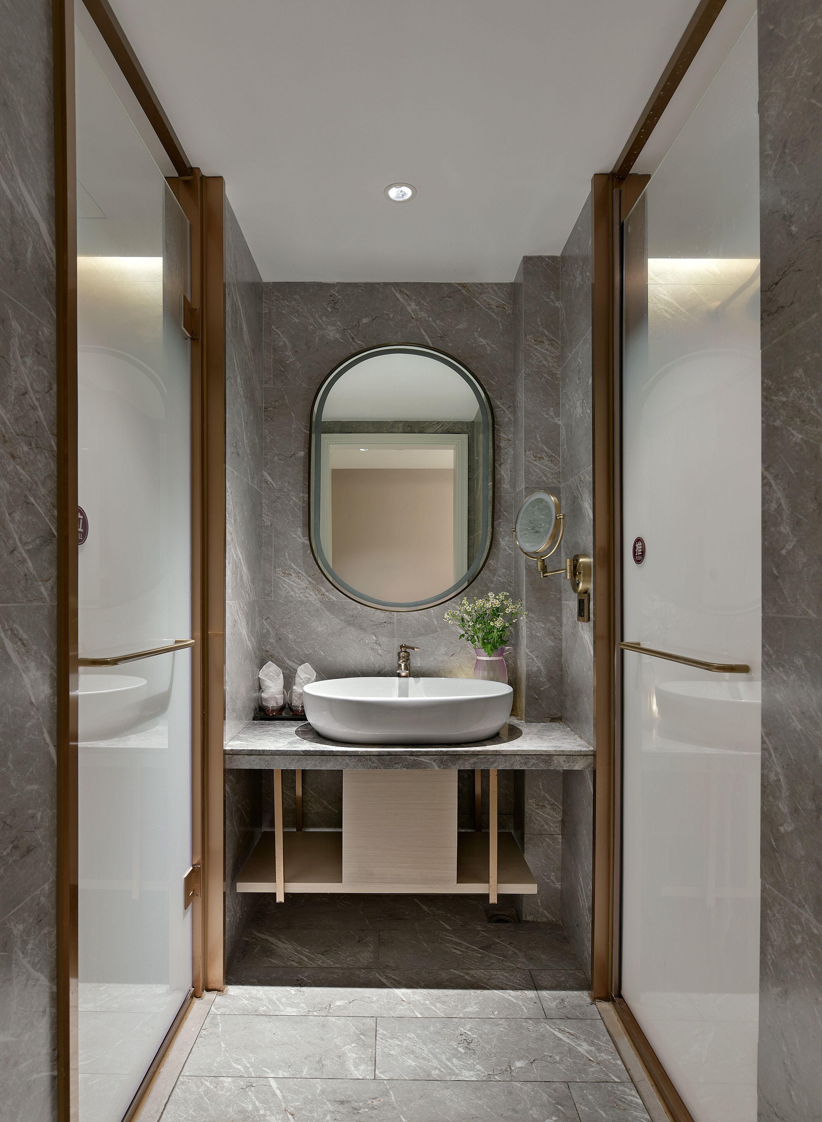 A modern bathroom with a large oval sink, a round mirror, and a small vase with flowers.
