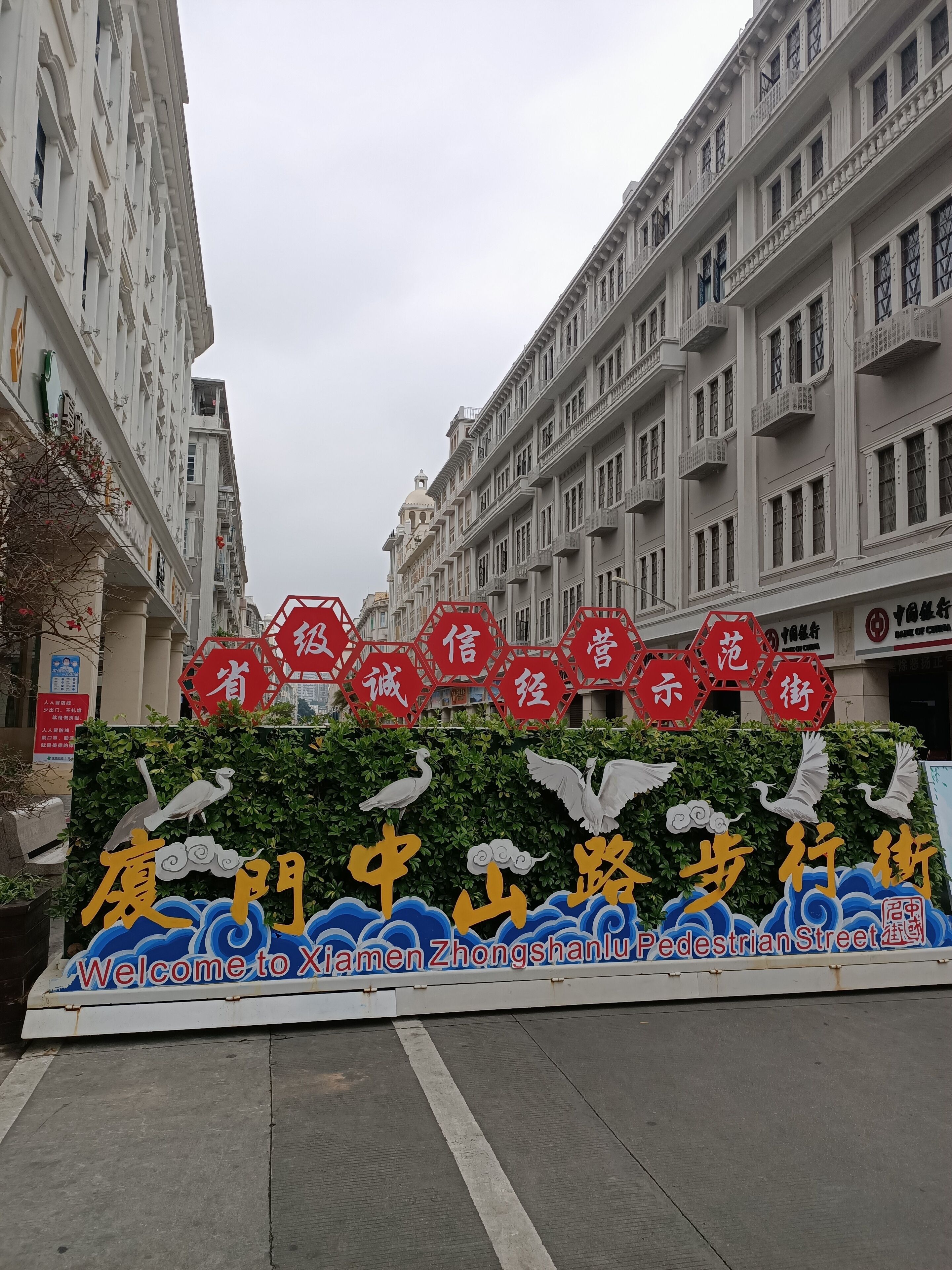 A pedestrian street entrance with a decorative sign featuring birds and clouds, surrounded by traditional buildings.