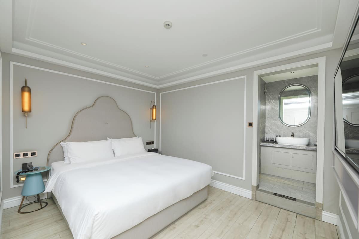 Une chambre d’hôtel dotée d’un grand lit, de tables de chevet, d’un bureau avec une chaise, d’une salle de bain avec un lavabo et un miroir, et d’un dressing.