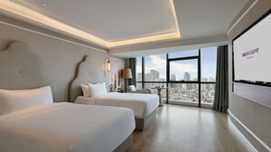 Habitación de hotel con dos camas, vistas a la ciudad y un ventanal grande.