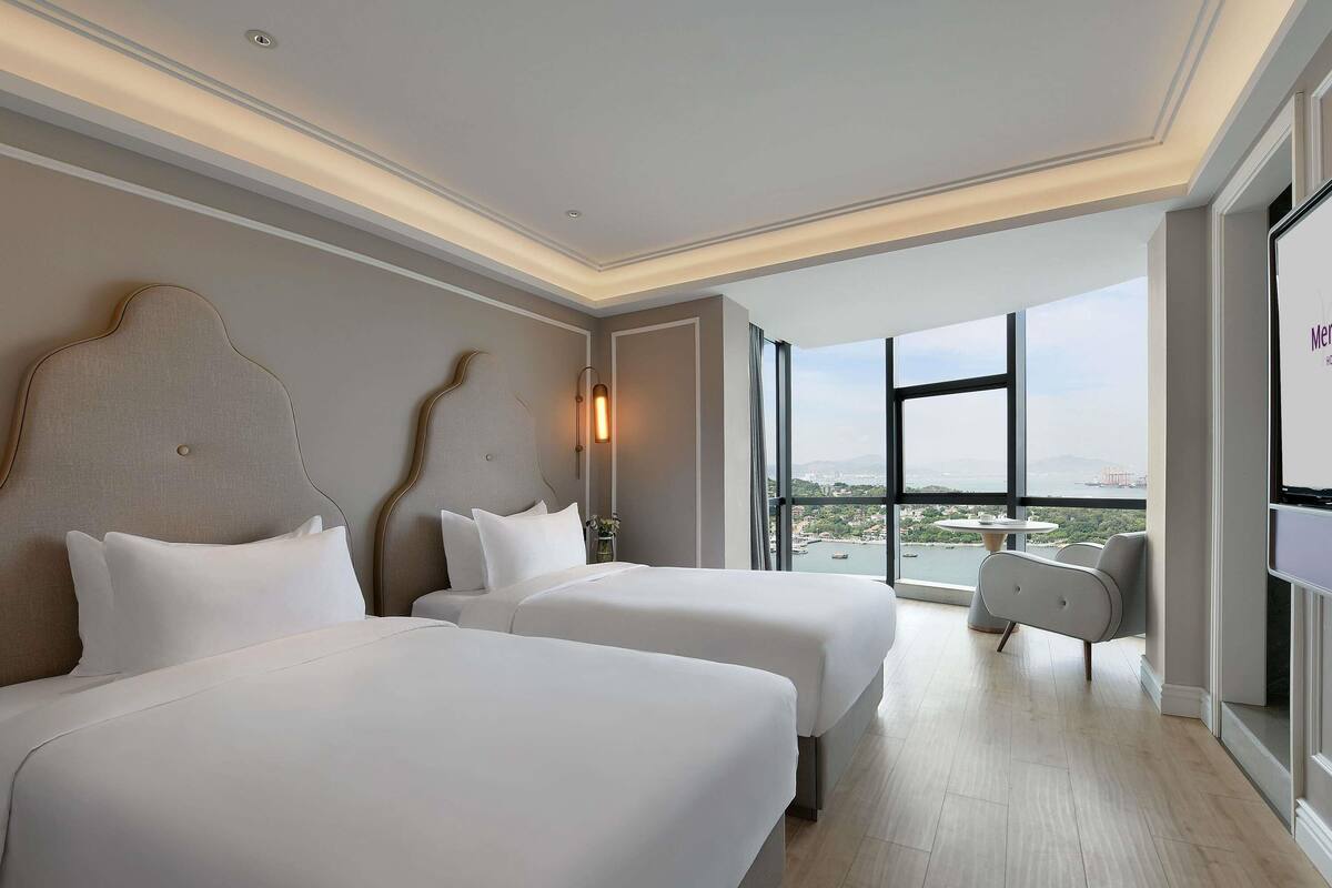 Une chambre d’hôtel avec deux lits, une grande fenêtre donnant sur la ville et un design moderne.