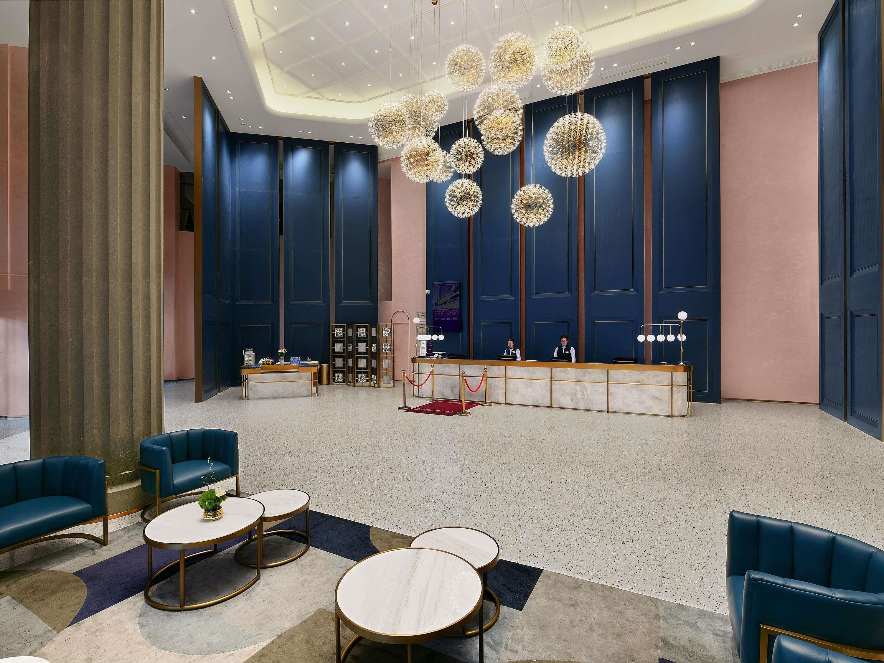 Een moderne lobby met een receptiebalie, een zithoek en decoratieve verlichting.