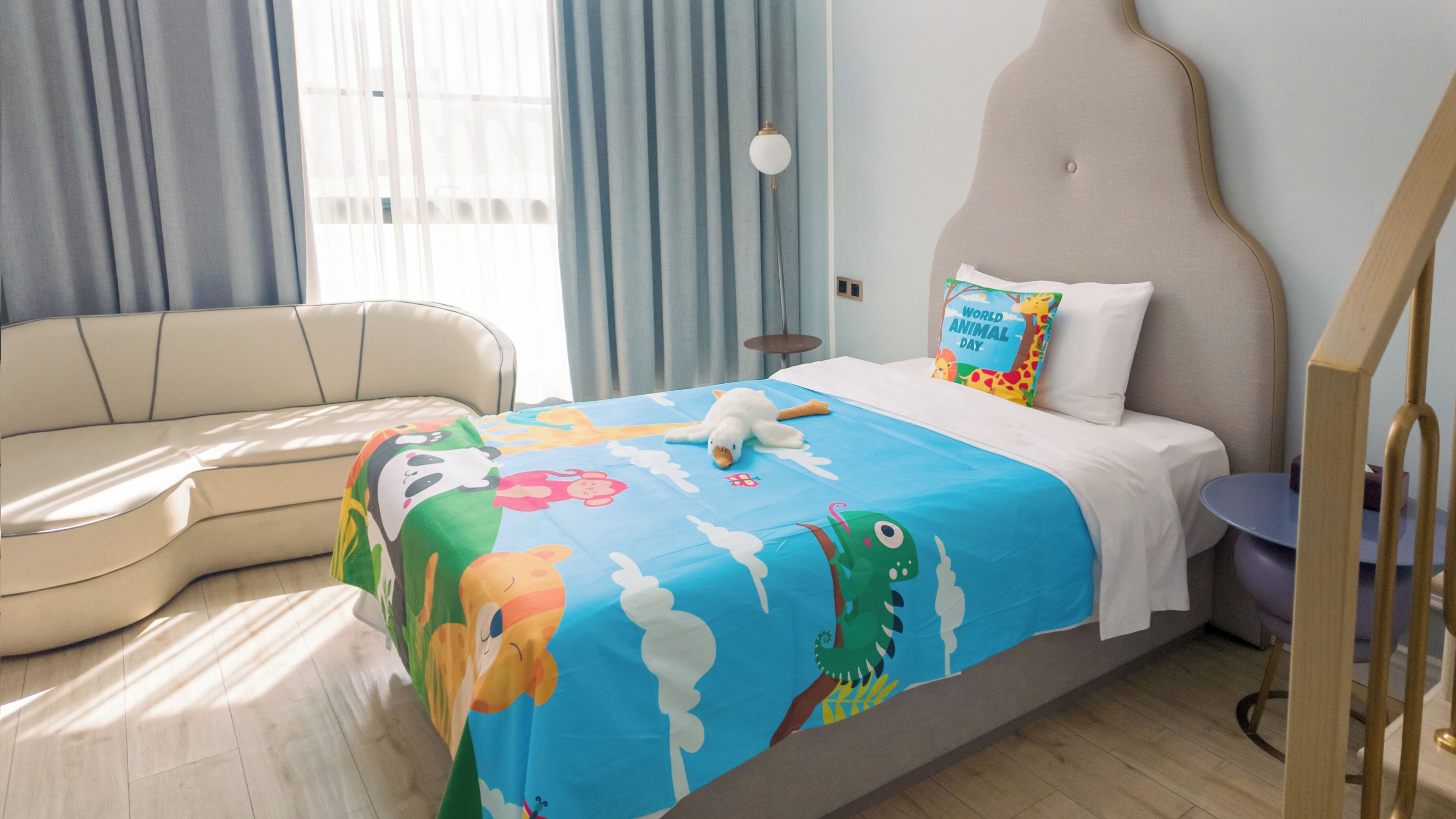 Una habitación de hotel con cama, sofá, lámpara y ventana con cortinas.
