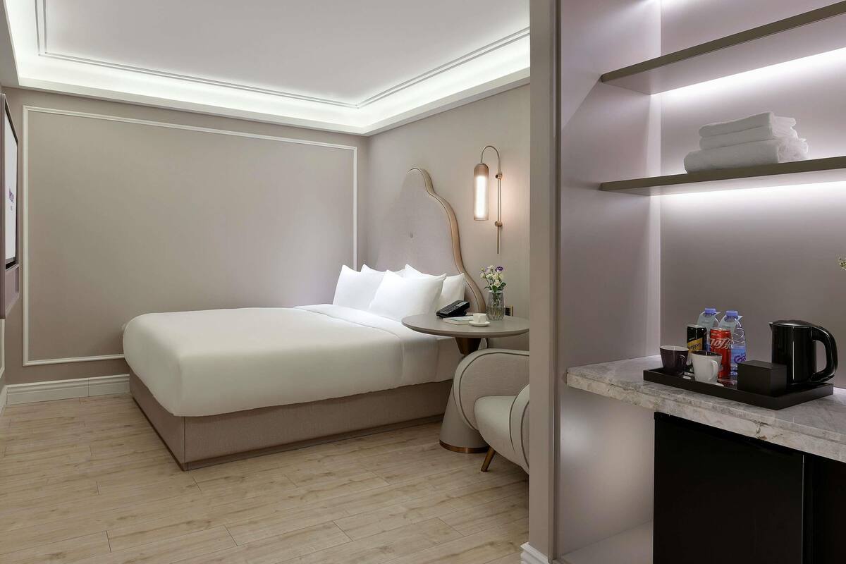 Une chambre d’hôtel comprenant un lit, une table de chevet, une chaise et un petit bureau avec une bouilloire et des tasses.