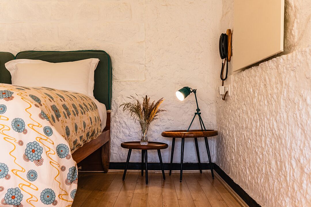 Et soveværelse med en seng, et lille bord med en lampe og en telefon ophængt på væggen.