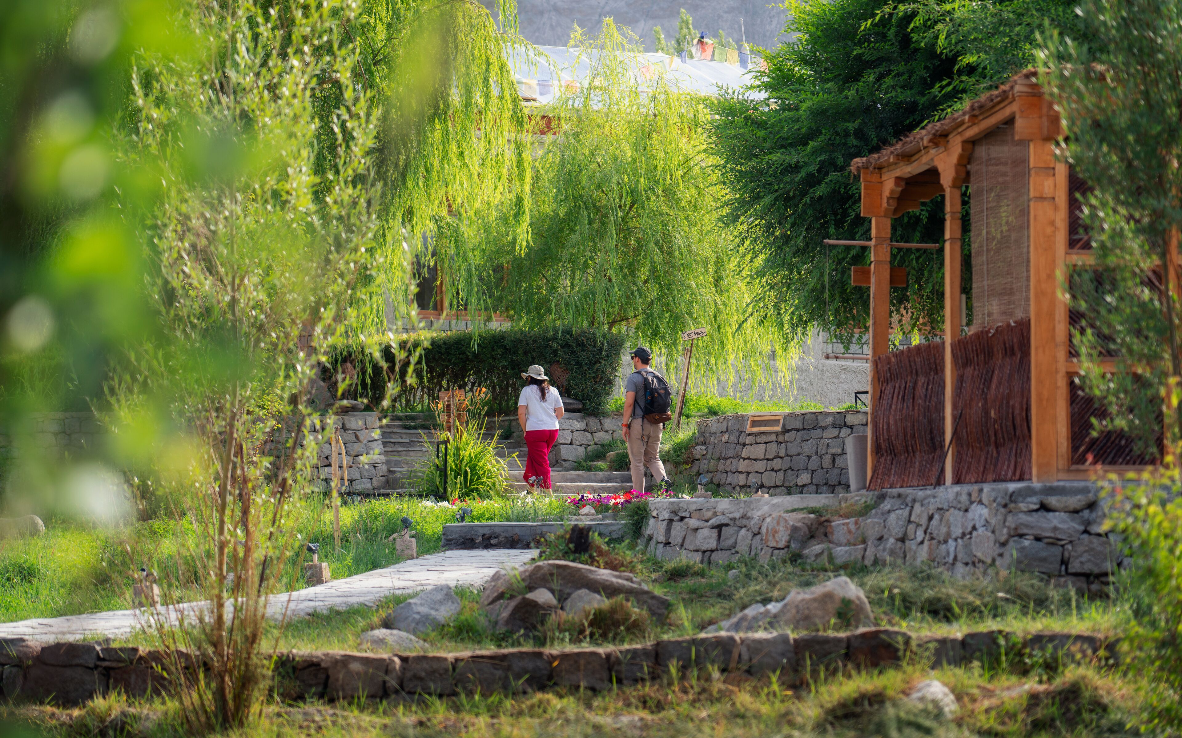 A stone pathway leading to a wooden structure with a stone wall and greenery.