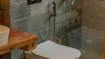 Un baño con pared de piedra, un inodoro, ducha y estante de madera.