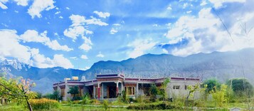 Un edificio tradicional con techo plano y balcón, rodeado de montañas y vegetación.