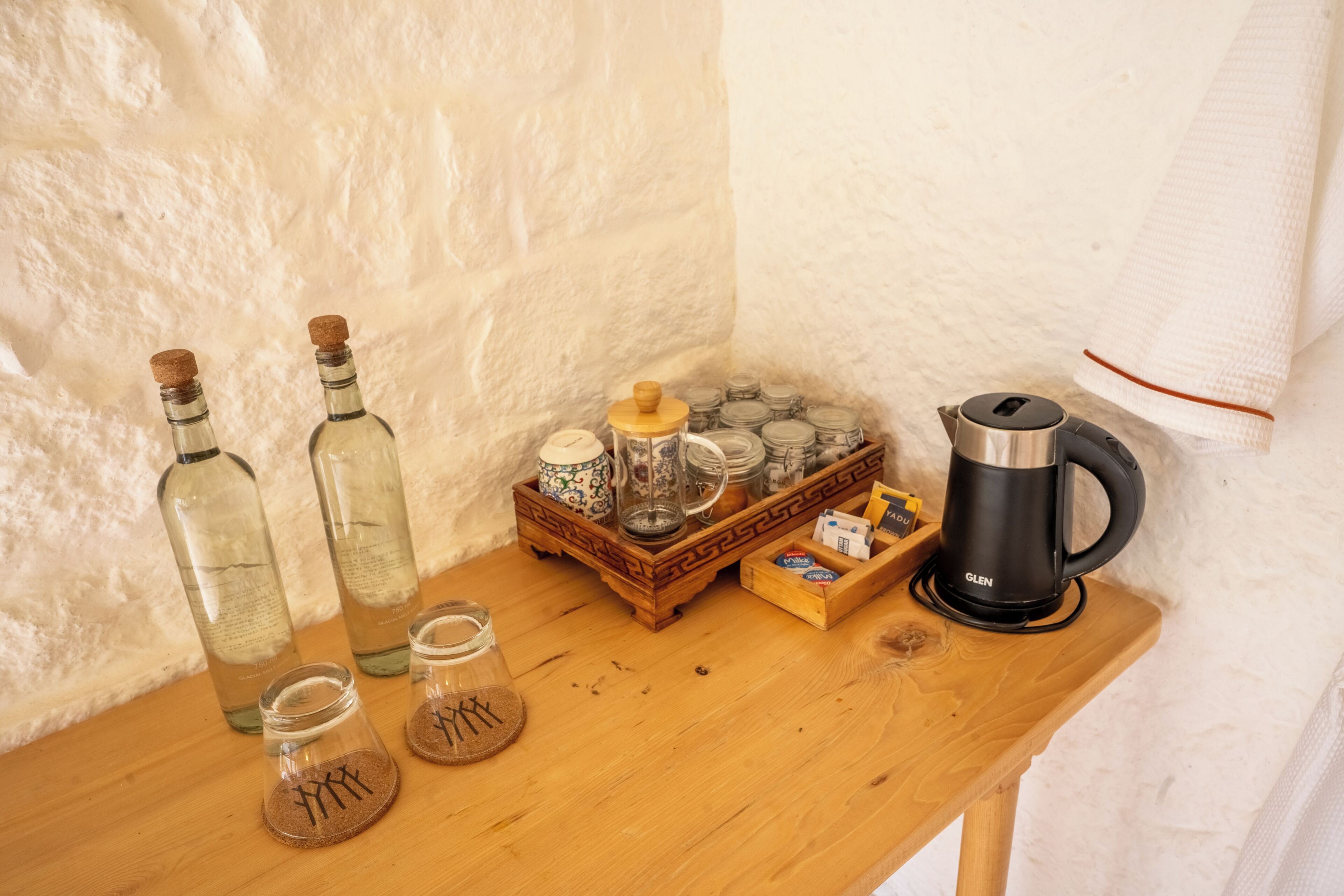 Una mesa de madera con varios utensilios de cocina, incluyendo botellas, frascos, una cafetera y una bandeja con recipientes.