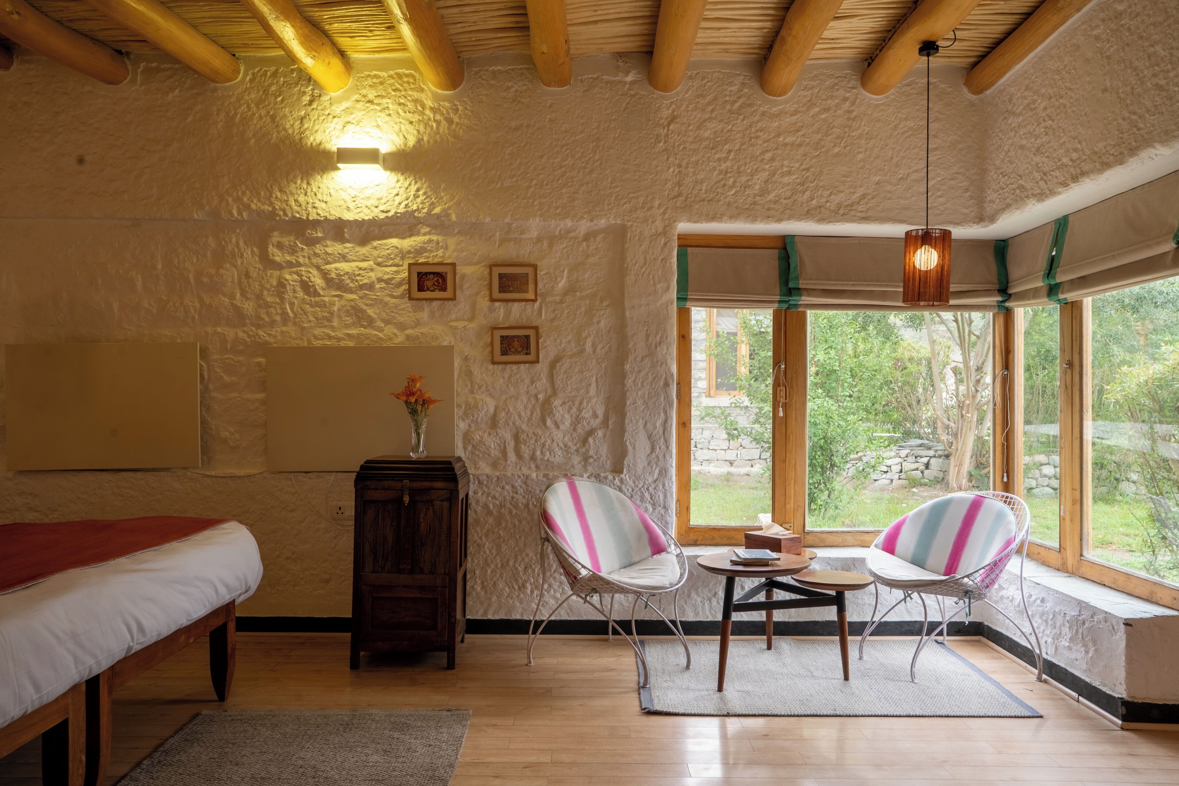 Ein Zimmer mit einem Bett, zwei Stühlen, einem kleinen Tisch, einer Vase mit Blumen und einem Fenster mit Blick auf Grünflächen.