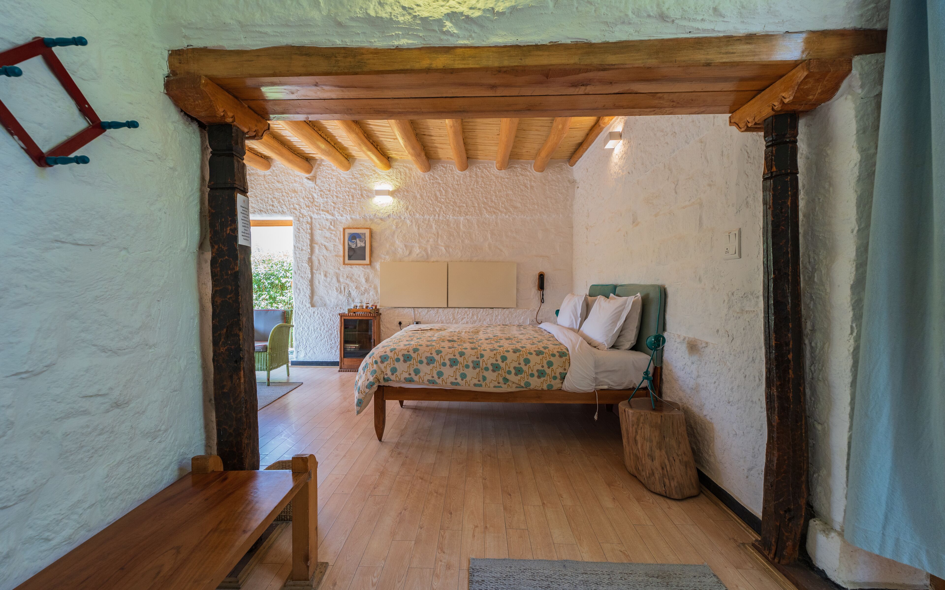 Ein rustikales Schlafzimmer mit Holzbalkendecke, einem Bett mit gemustertem Überwurf, einem grünen Sessel und einer Holzbank.