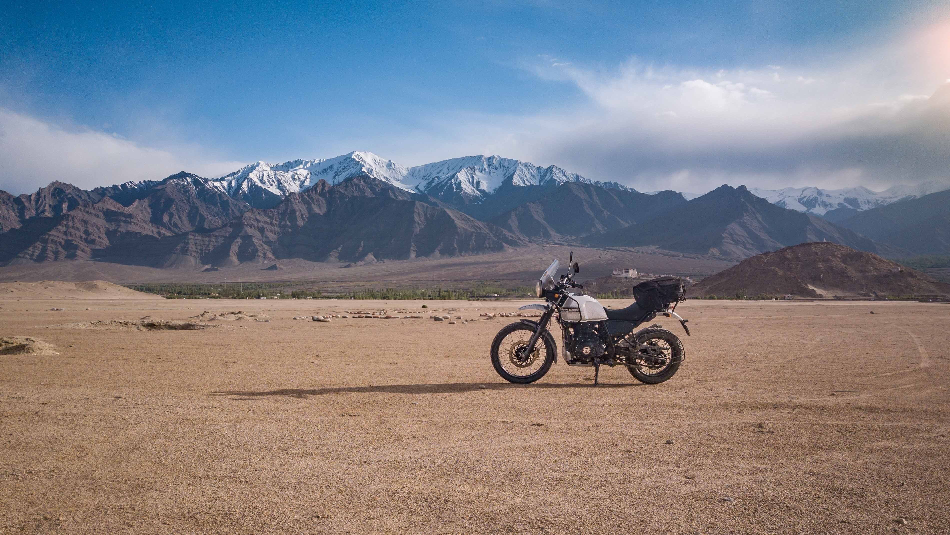 Ein Motorrad in einer kargen Landschaft, im Hintergrund verschneite Berge.