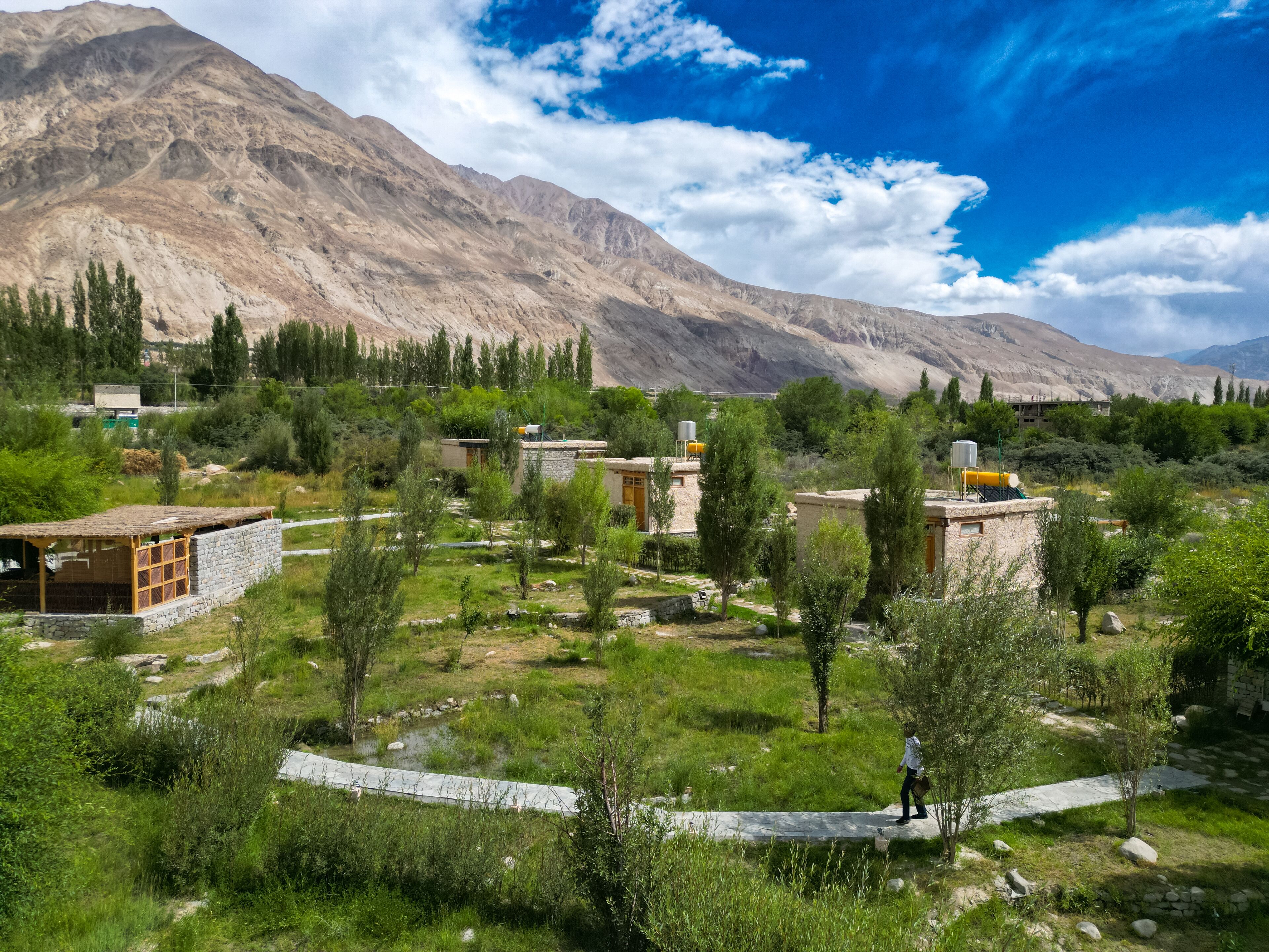 A mountainous landscape with traditional stone buildings, a paved path, and sparse vegetation.