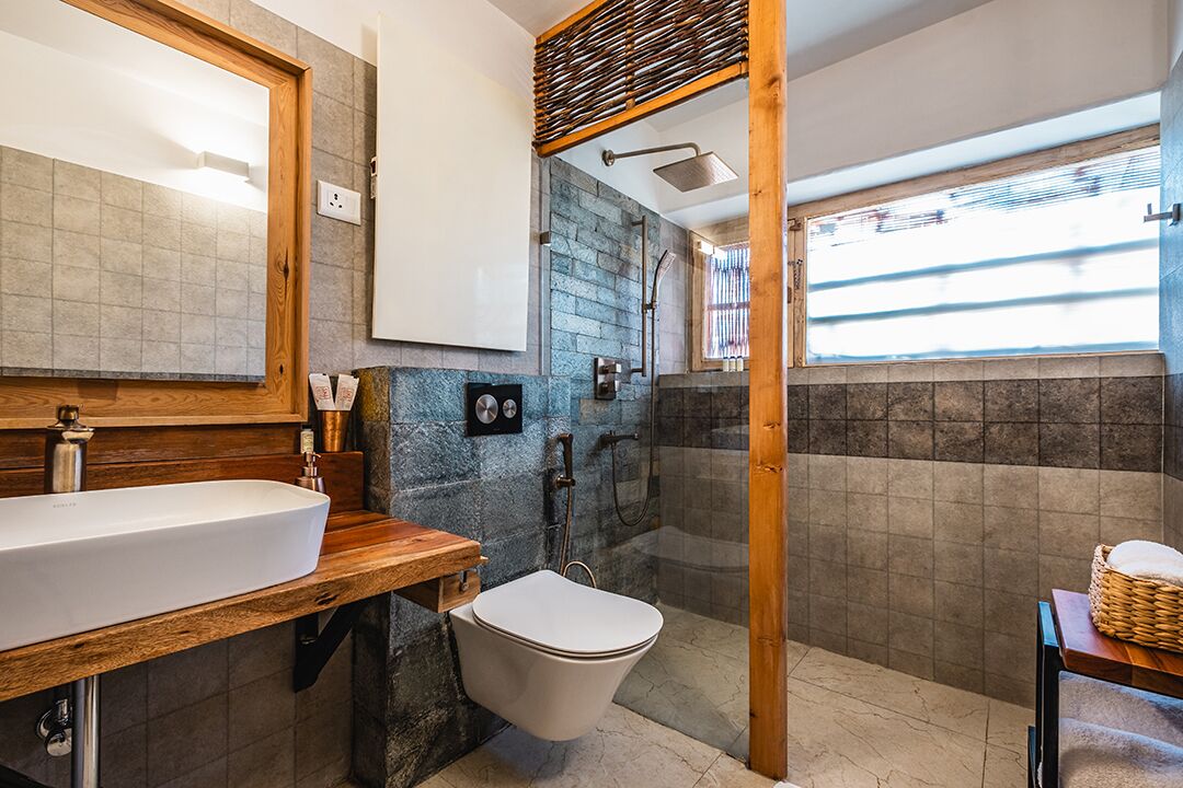 Un baño moderno con un espejo grande, encimera de madera, lavabo blanco y zona de ducha con pared de piedra.
