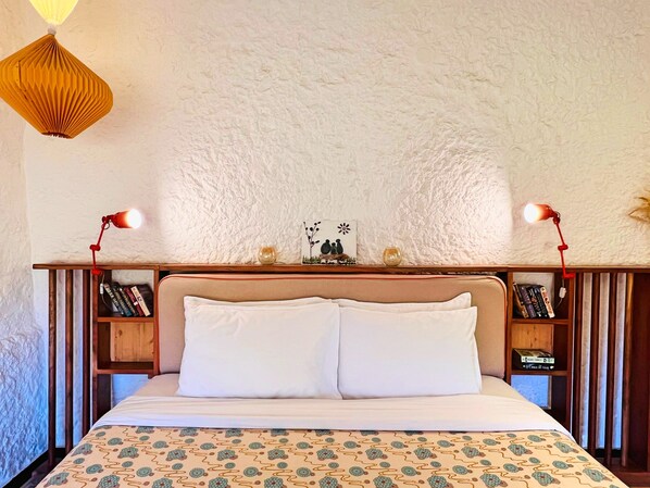Una cama bien hecha con sábanas blancas y un edredón estampado, flanqueada por dos mesitas de noche con libros y objetos decorativos.