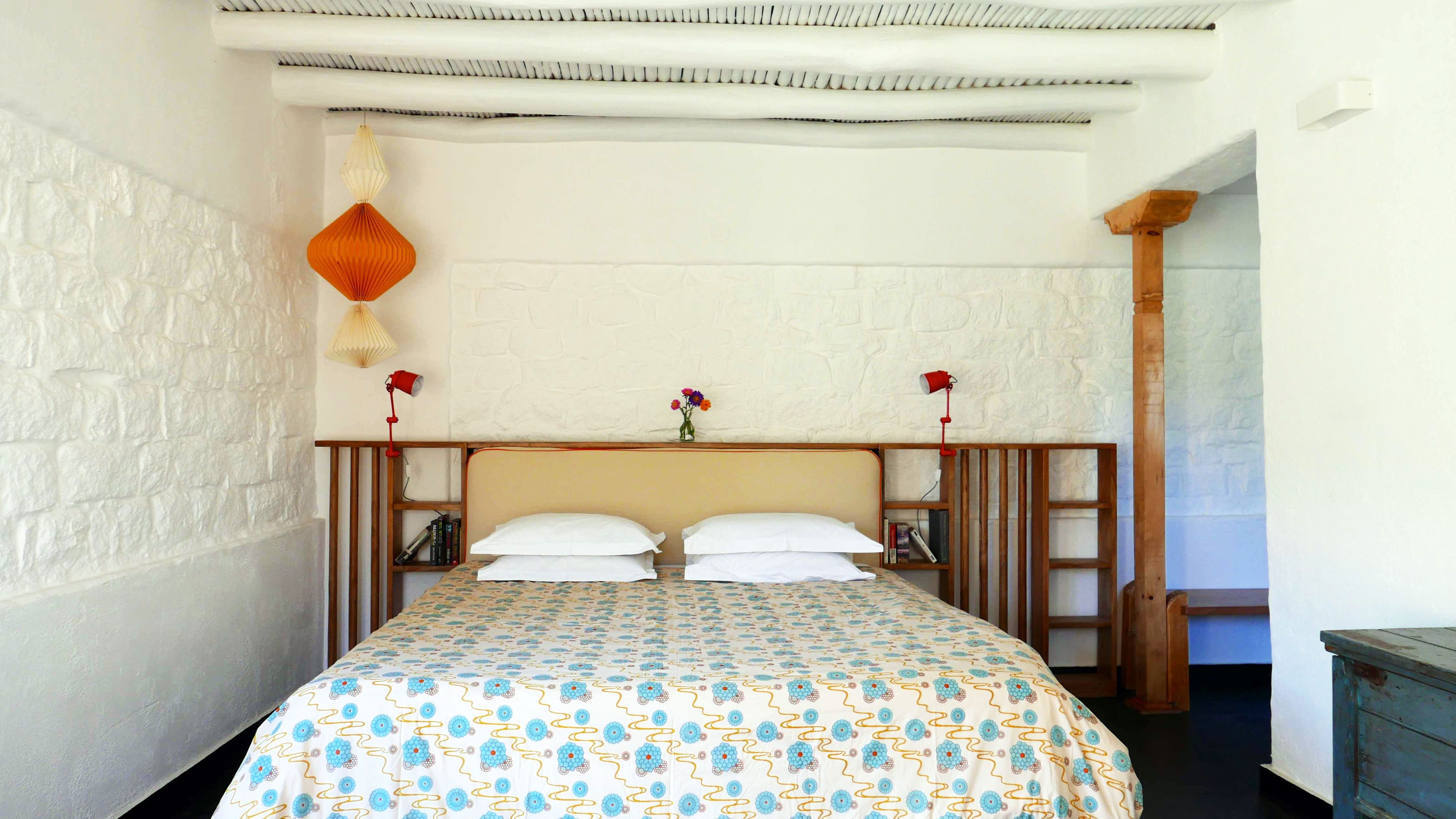 Un dormitorio con una cama, dos mesitas de noche, una lámpara colgante y un pequeño florero con flores.