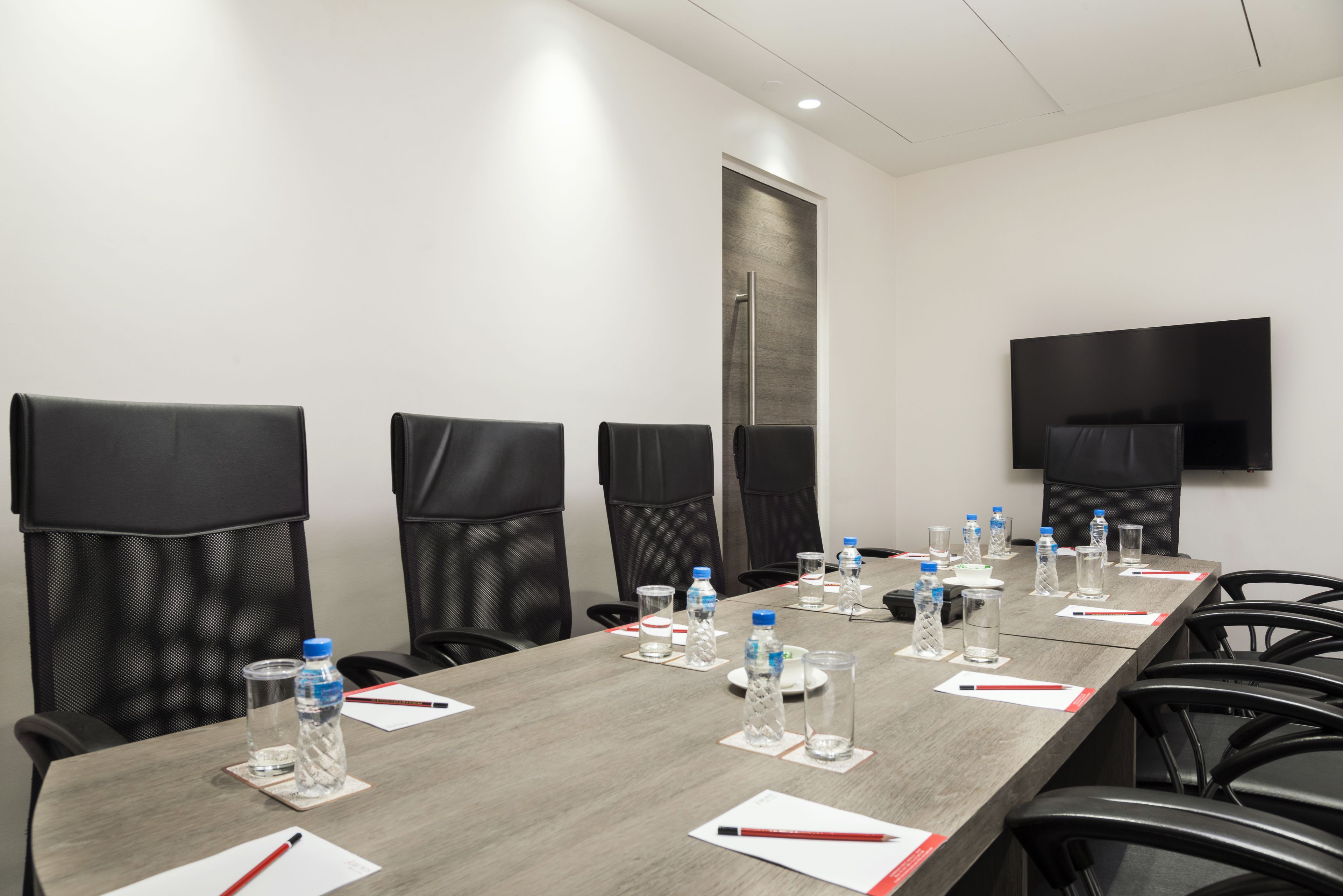 A conference room with a long table, chairs, water bottles, glasses, and a TV mounted on the wall.