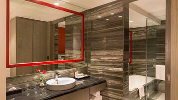 A modern bathroom with a large mirror, marble walls, a round sink, and a glass-enclosed shower.