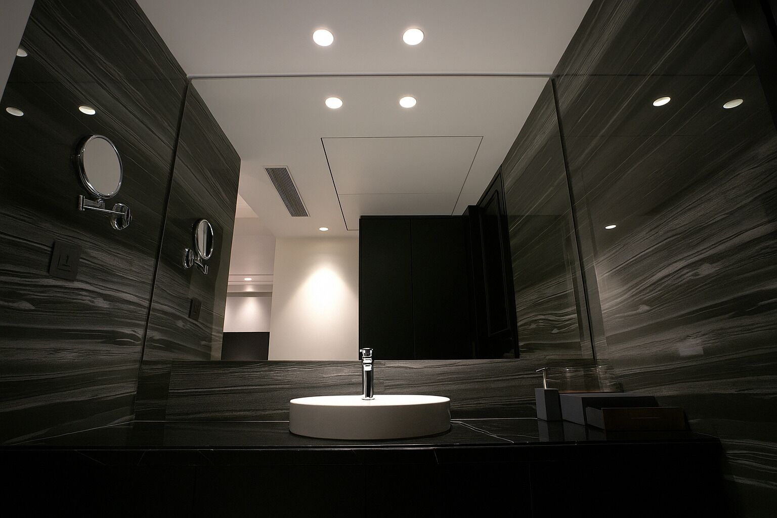 A modern bathroom with a round sink, mirrored walls, and recessed ceiling lights.