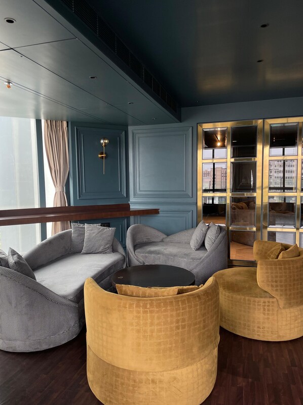 A modern lounge area with a blue wall, a round table, and two yellow armchairs. - Aauris (Kolkata)