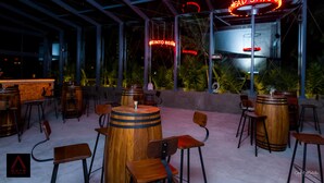 An outdoor bar area with wooden barrels as tables, bar stools, and a neon sign. - Aauris (Kolkata)