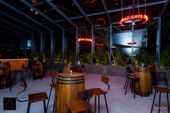 An outdoor bar area with wooden barrels as tables, bar stools, and a neon sign. - Aauris (Kolkata)