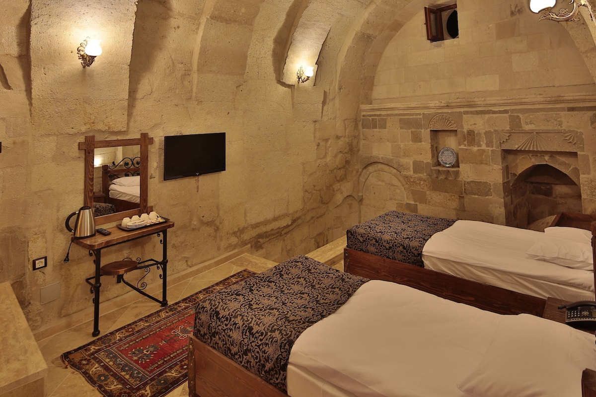 Ein Zimmer mit zwei Betten, einem Holztisch mit Wasserkocher, einem Spiegel und einem Kamin.