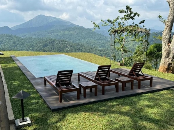A swimming pool with lounge chairs and a pergola, surrounded by a grassy area and mountains in the background.