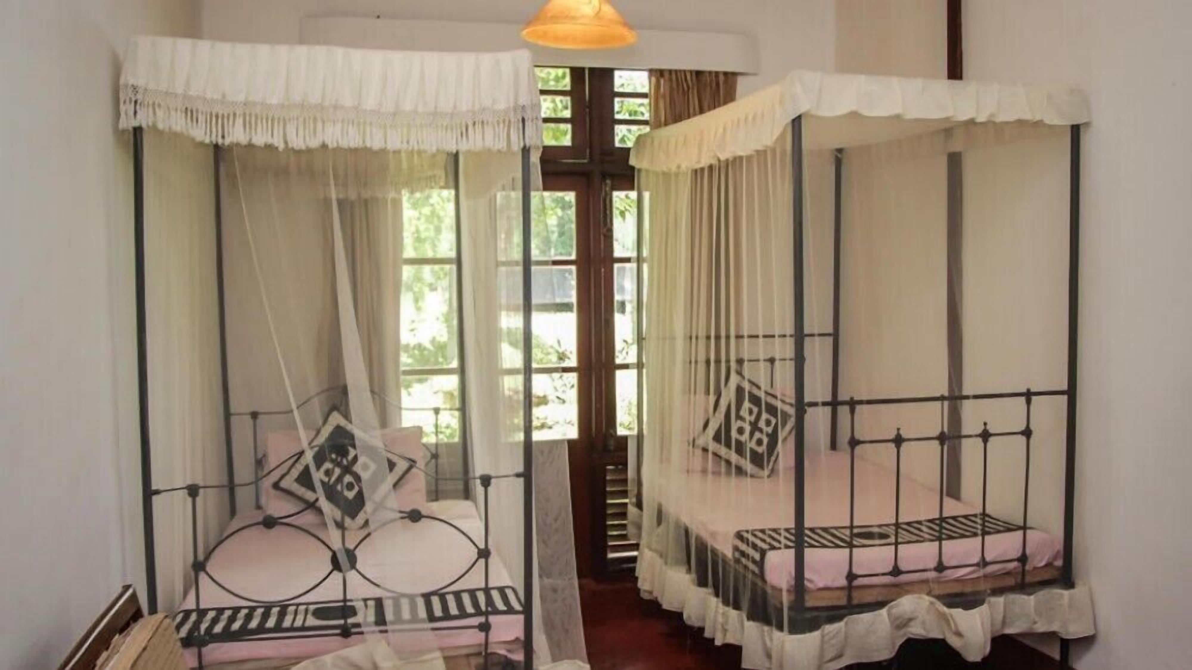 A room with two single beds, each with a canopy and a metal frame.