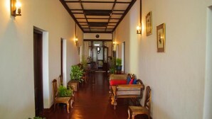 A corridor with wooden flooring, chairs, and tables, leading to a room with a wooden ceiling and a door at the end.