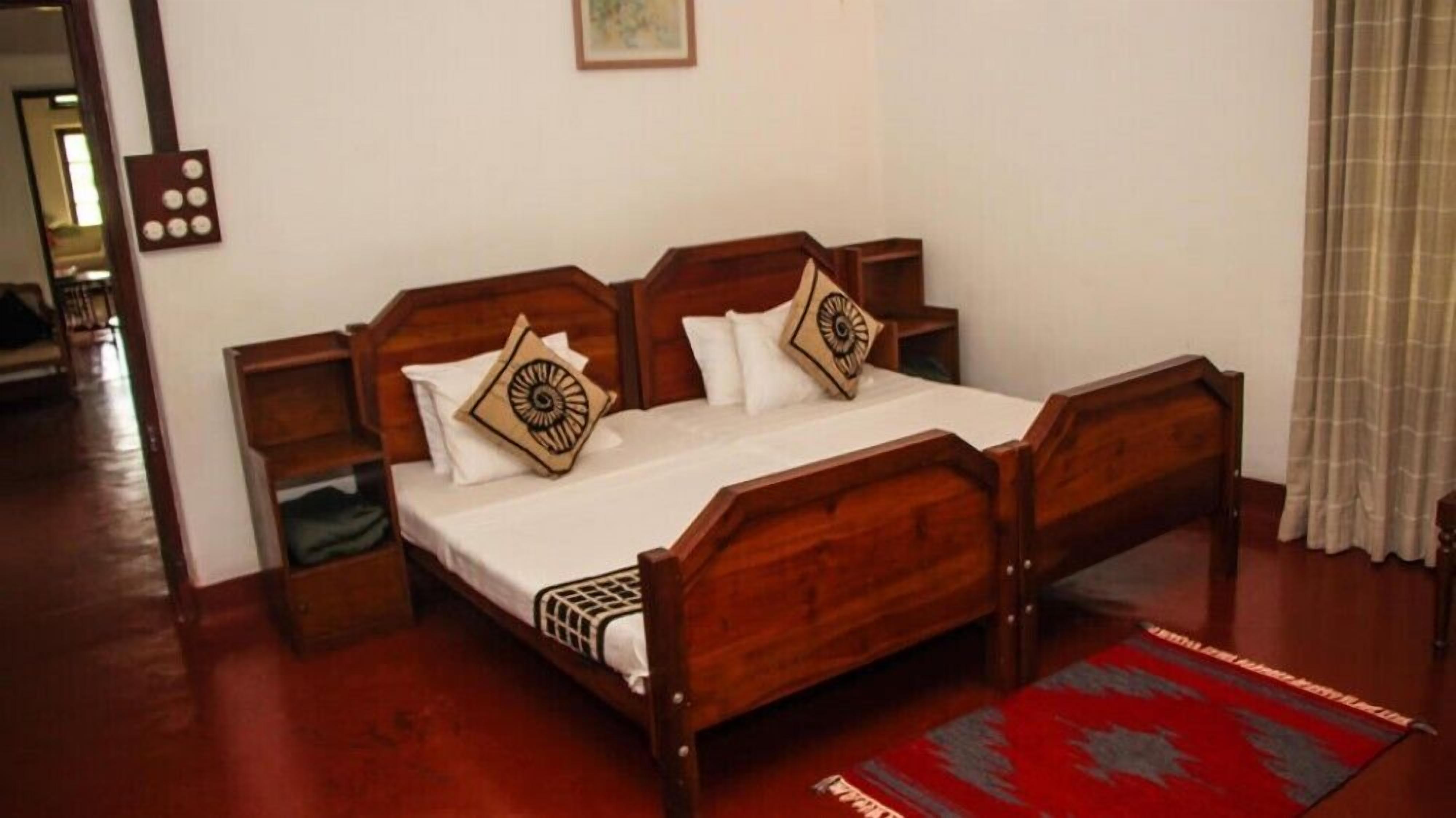 Ein hölzernes Himmelbett mit weißen Leinen und gemusterten Kissen, ein Nachttisch aus Holz und ein Teppich im Rot-Grau-Design.