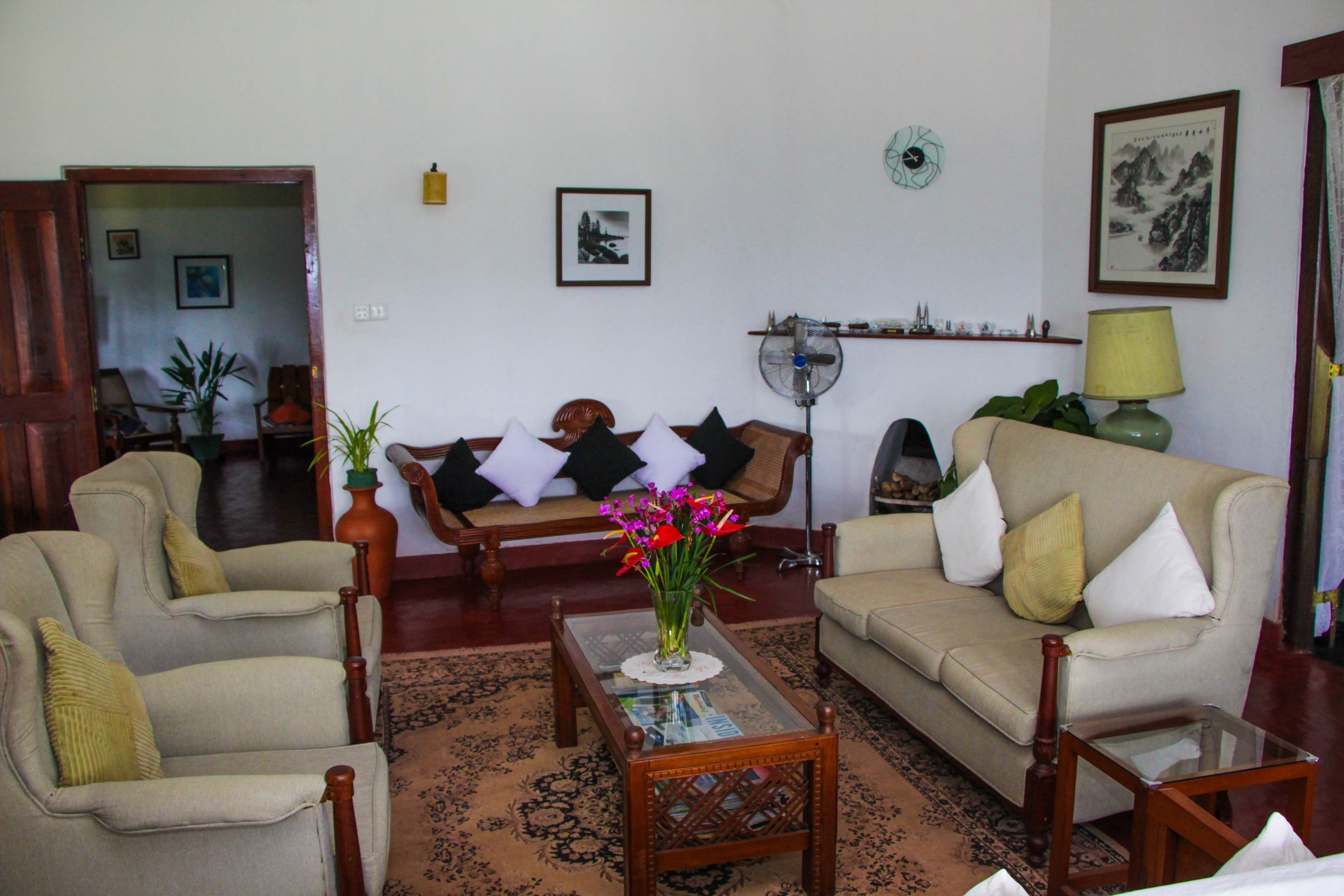 A living room with a sofa, armchairs, a coffee table, and a fan.