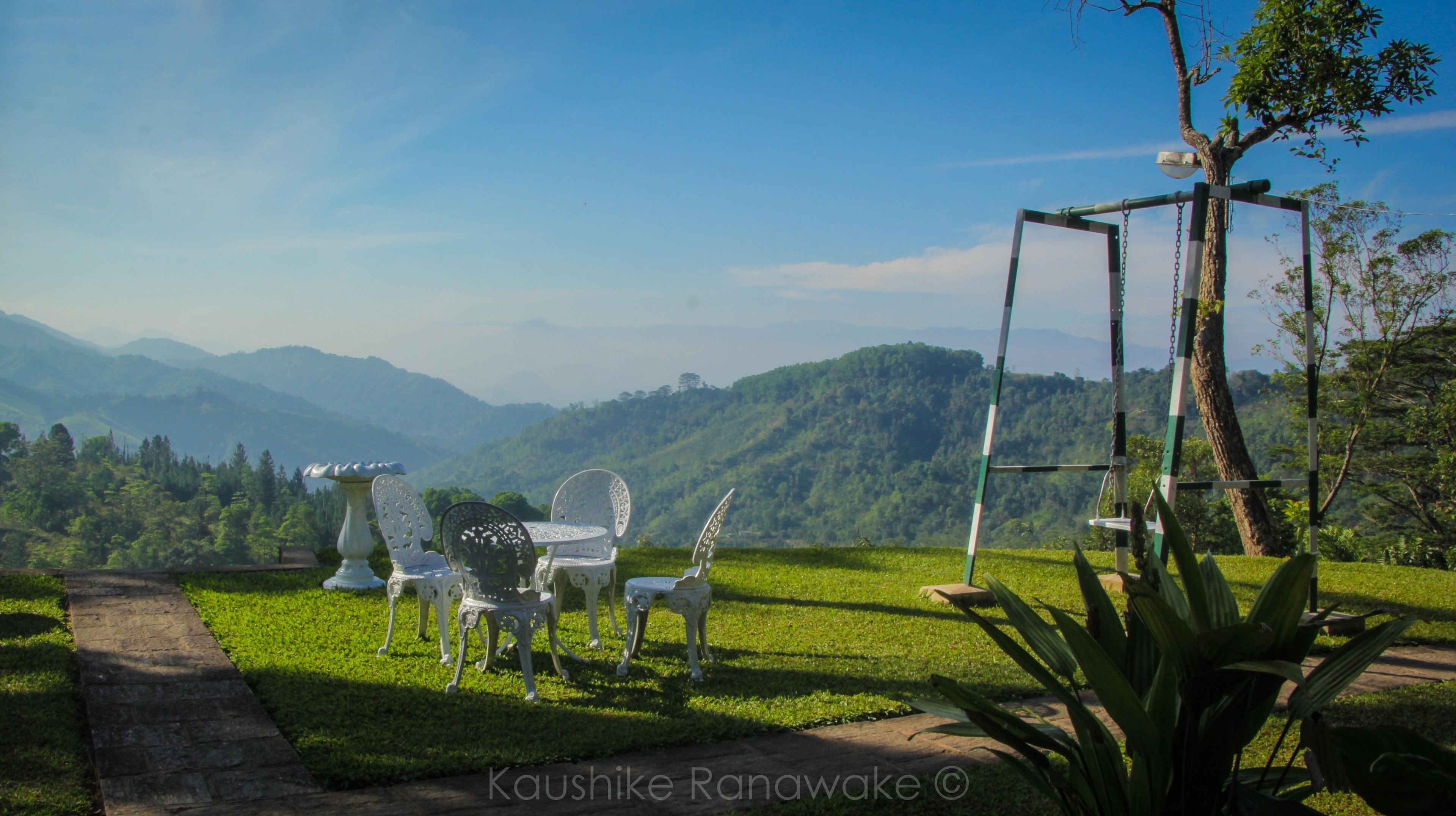 A garden with a table and chairs, a swing set, and a view of mountains.