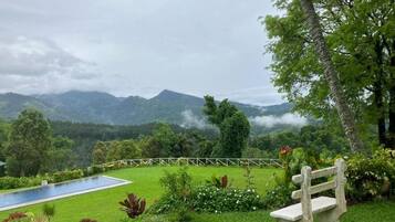 Un jardin luxuriant avec une piscine, un banc et une vue sur les montagnes.